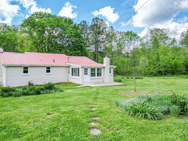 rear view of property featuring a chimney, a patio, metal roof, and a yard