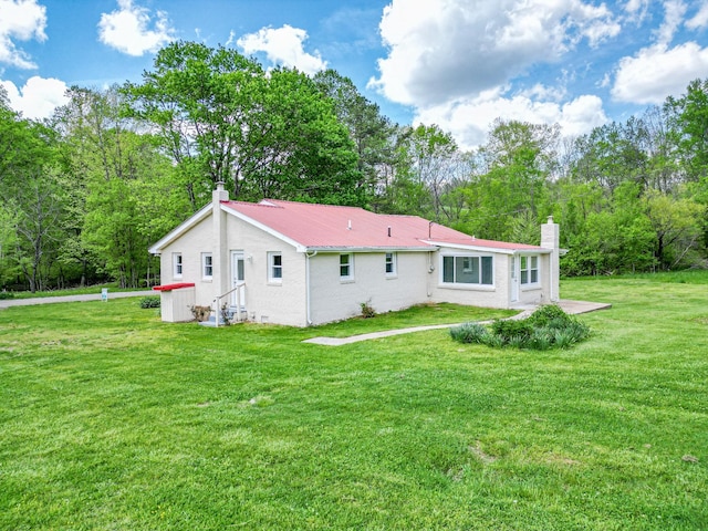 back of house featuring a chimney, brick siding, metal roof, and a lawn