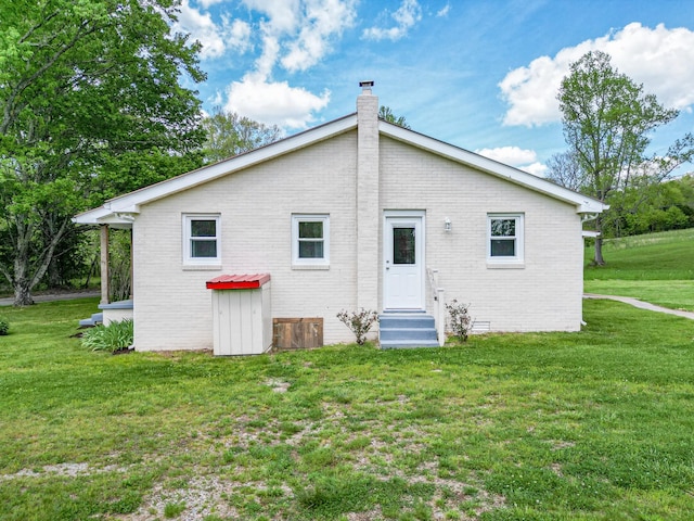 rear view of property featuring a lawn, a chimney, entry steps, and brick siding
