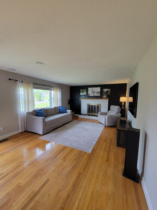 living room featuring baseboards, a fireplace, light wood finished floors, and visible vents
