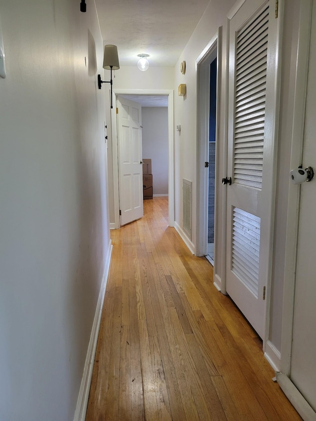 hall with light wood-type flooring, baseboards, and visible vents