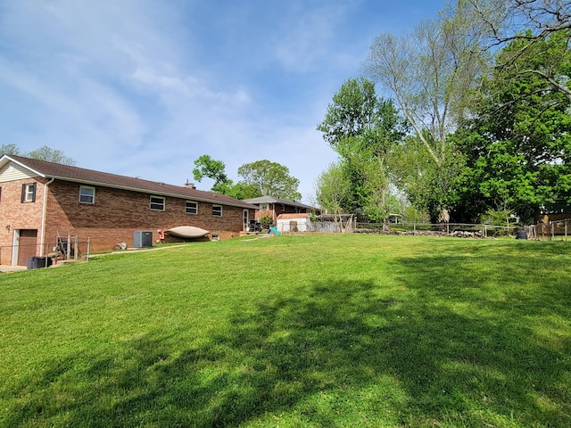 view of yard featuring fence, central air condition unit, and an attached garage