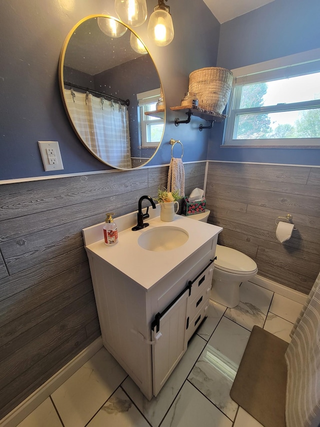 full bath featuring vanity, toilet, wood walls, marble finish floor, and a wainscoted wall