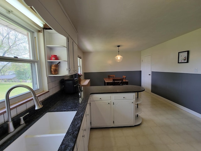 kitchen featuring a sink, dark countertops, open shelves, and a peninsula