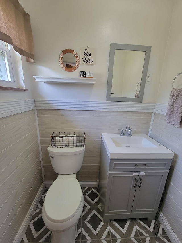 bathroom featuring toilet, tile walls, a wainscoted wall, and vanity