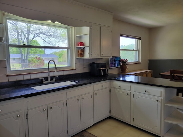 kitchen with a sink, dark countertops, white cabinets, and open shelves