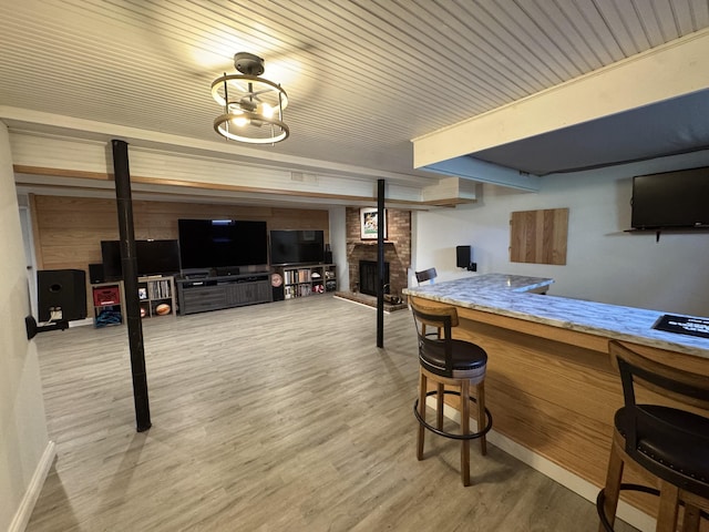 bar with light wood-type flooring, baseboards, a brick fireplace, and wood ceiling
