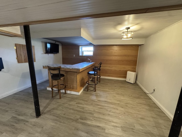 bar featuring baseboards, a dry bar, wood walls, and light wood-type flooring