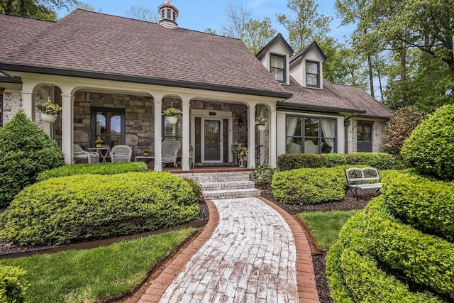 view of exterior entry featuring roof with shingles, a porch, and stone siding