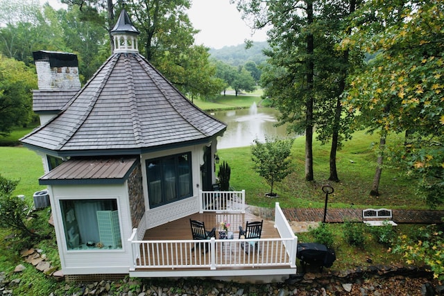 rear view of property featuring a chimney, a deck with water view, a yard, a gazebo, and central AC unit
