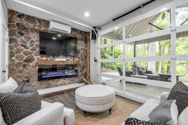 living room featuring wood finished floors, plenty of natural light, an AC wall unit, and a stone fireplace
