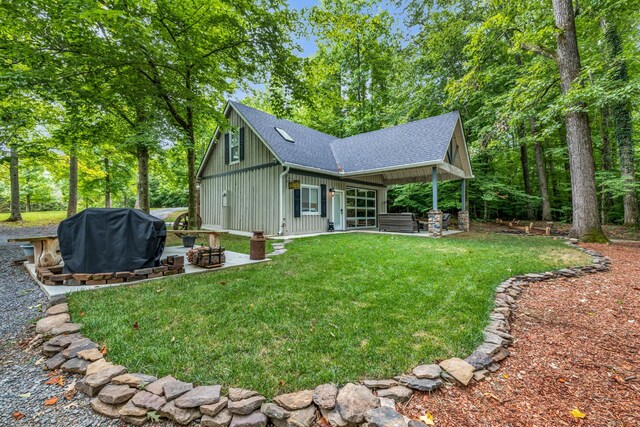 back of property with board and batten siding, a patio, a shingled roof, an outdoor fire pit, and a lawn