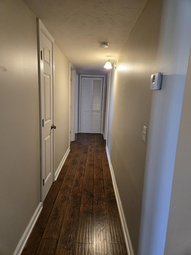 hallway featuring baseboards, hardwood / wood-style flooring, and a textured ceiling