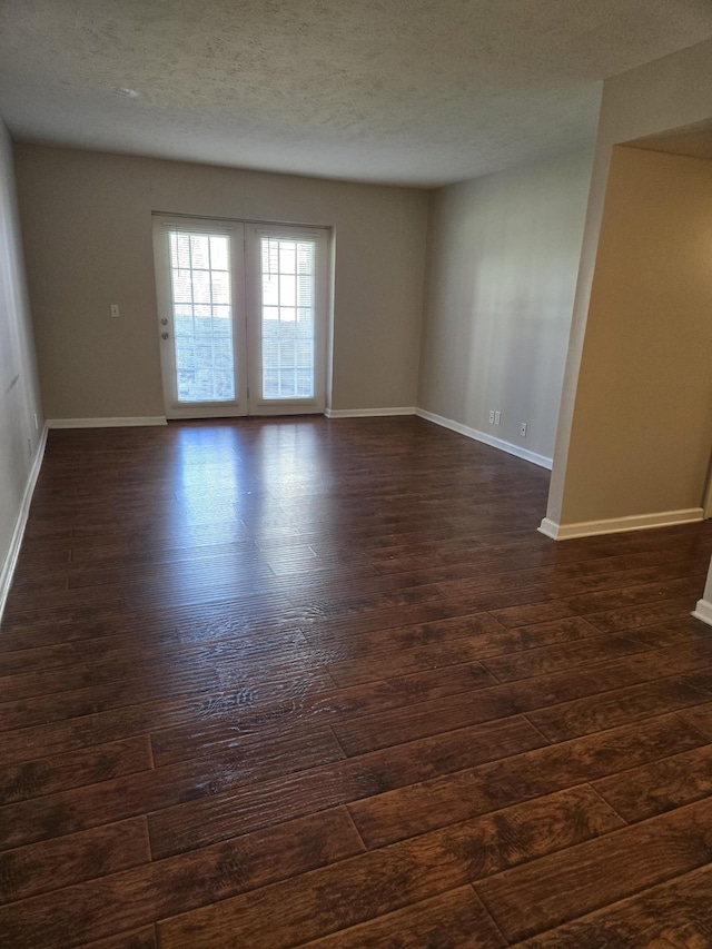 spare room with a textured ceiling, dark wood-style floors, and baseboards