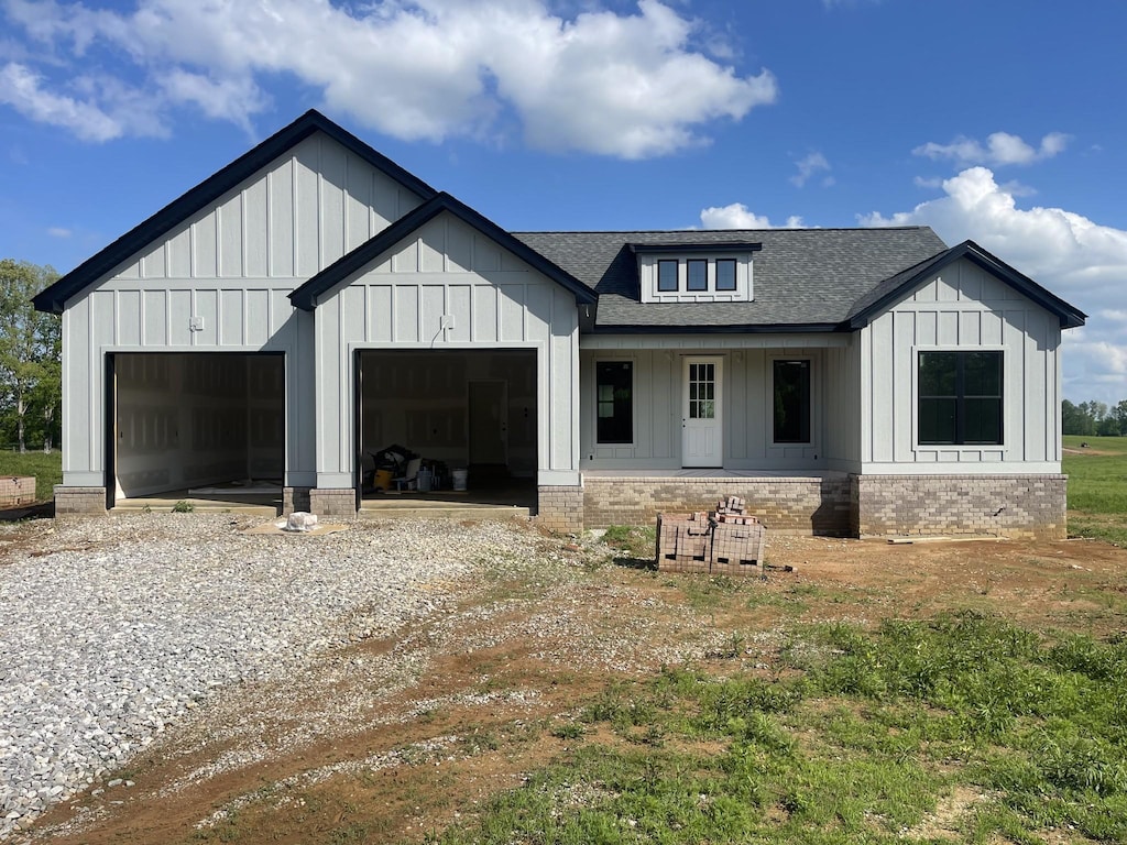modern inspired farmhouse featuring a garage, board and batten siding, gravel driveway, and a shingled roof
