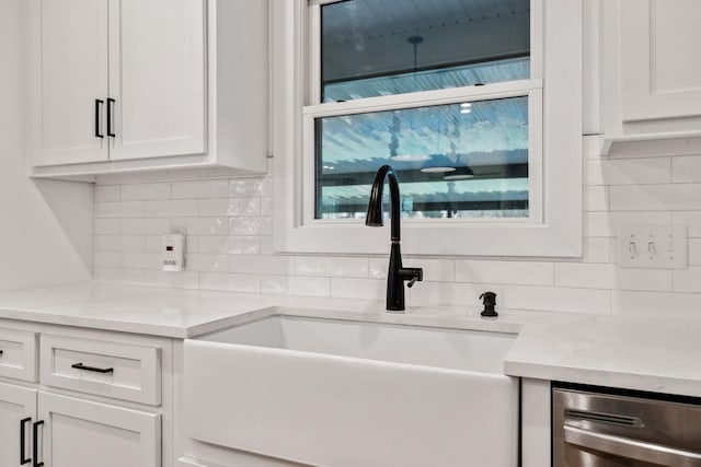 kitchen featuring light stone countertops, a sink, backsplash, white cabinetry, and stainless steel dishwasher