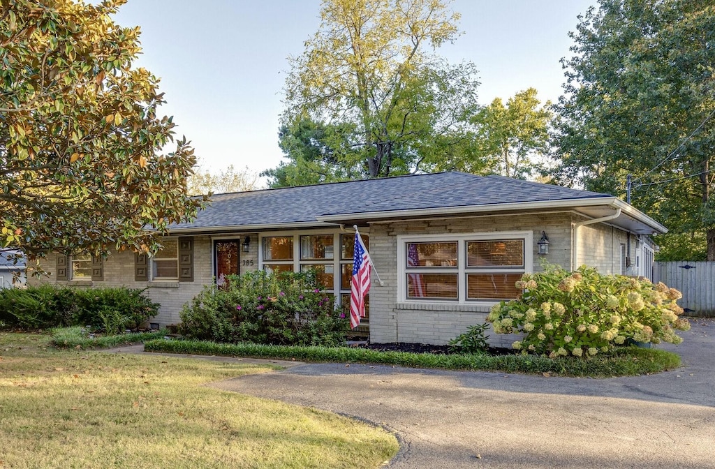 ranch-style home featuring brick siding, a shingled roof, and a front yard