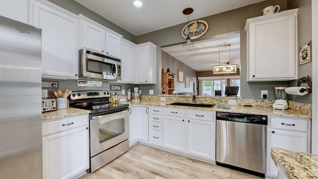 kitchen featuring a sink, stainless steel appliances, light wood-style floors, decorative light fixtures, and white cabinets