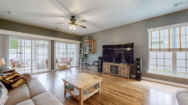 living room with a ceiling fan, visible vents, wood finished floors, and baseboards