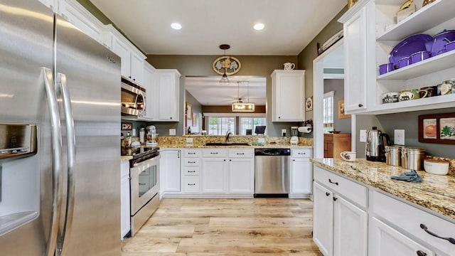 kitchen featuring light stone countertops, a sink, light wood-style flooring, white cabinets, and appliances with stainless steel finishes
