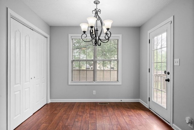 unfurnished dining area featuring visible vents, baseboards, a chandelier, and dark wood-type flooring