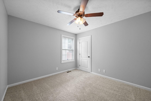 unfurnished room with light colored carpet, ceiling fan, baseboards, visible vents, and a textured ceiling