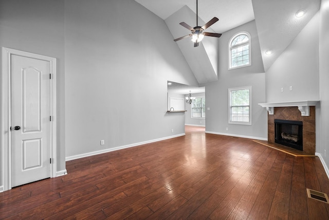 unfurnished living room with a tiled fireplace, hardwood / wood-style flooring, ceiling fan with notable chandelier, visible vents, and high vaulted ceiling