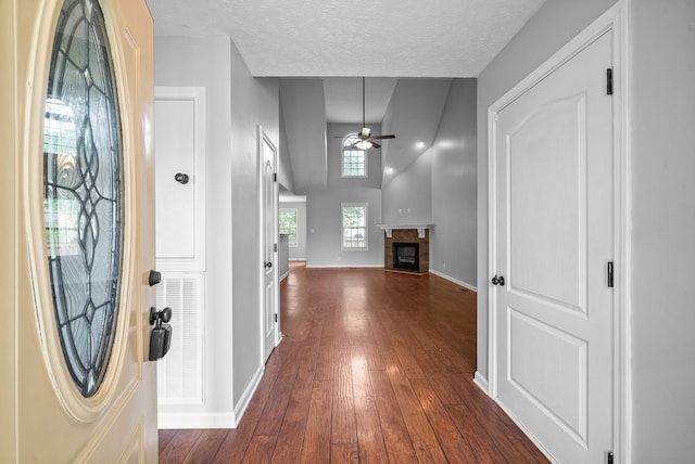 entryway with a textured ceiling, dark wood-style floors, baseboards, a glass covered fireplace, and a ceiling fan