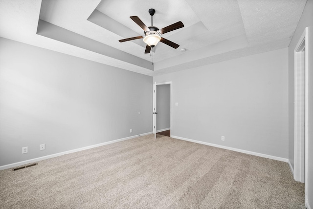 unfurnished bedroom with light colored carpet, visible vents, a raised ceiling, and baseboards