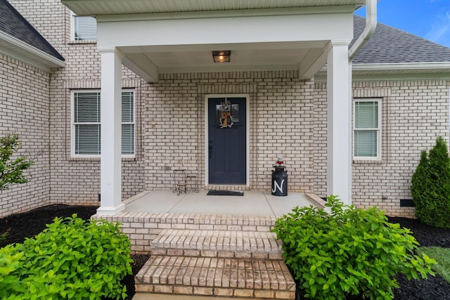 entrance to property with a porch, a shingled roof, and brick siding