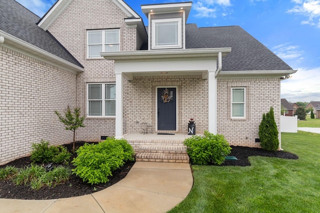 property entrance with crawl space, roof with shingles, a yard, and brick siding