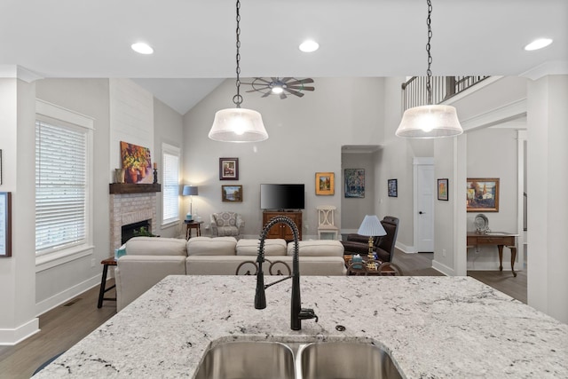 kitchen featuring a sink, a fireplace, ceiling fan, light stone counters, and open floor plan