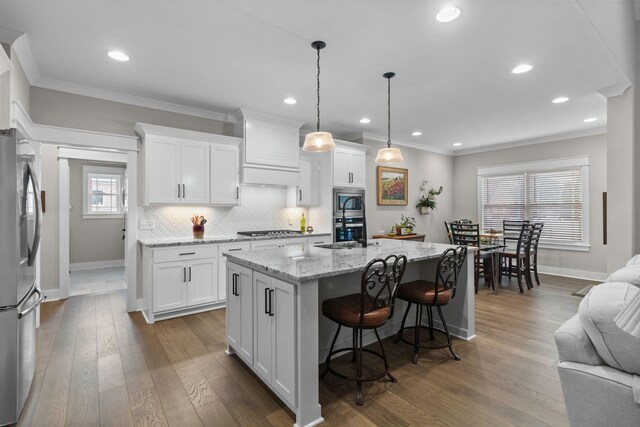 kitchen with a kitchen bar, ornamental molding, baseboards, premium range hood, and appliances with stainless steel finishes