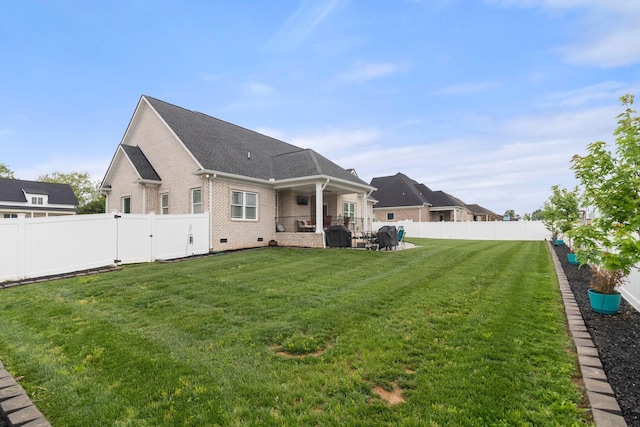 rear view of property with a shingled roof, a patio area, a fenced backyard, a lawn, and brick siding