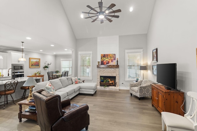 living area with light wood-style flooring, a large fireplace, recessed lighting, a ceiling fan, and high vaulted ceiling