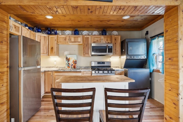 kitchen with light wood-type flooring, stacked washer / drying machine, appliances with stainless steel finishes, and wood ceiling