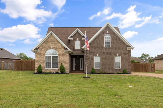 traditional-style house with a front lawn, stone siding, and fence