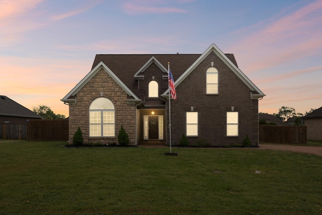 traditional-style home with fence, a front yard, and stone siding