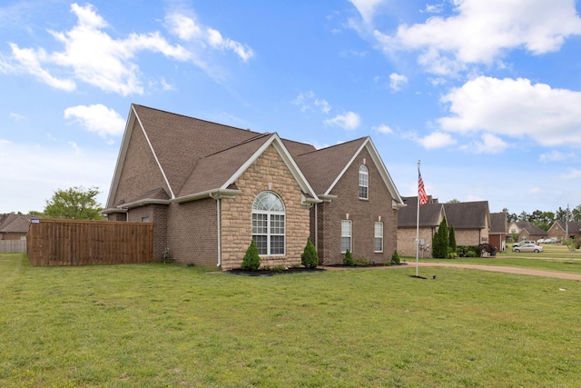 view of front of home featuring a front lawn, brick siding, stone siding, roof with shingles, and fence