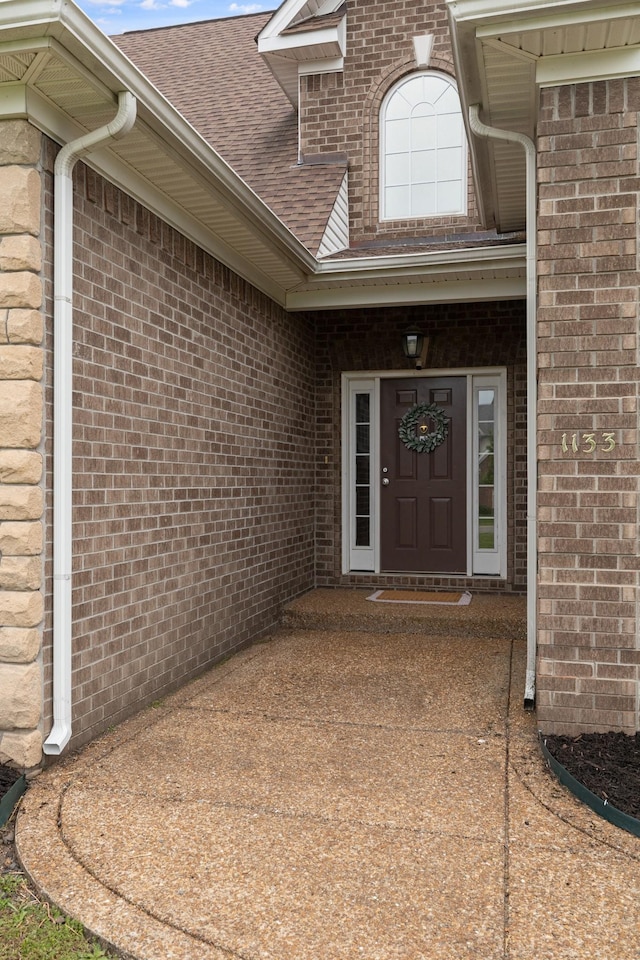 doorway to property with a shingled roof and brick siding