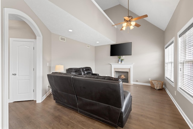 living area featuring a fireplace with flush hearth, ceiling fan, visible vents, baseboards, and wood finished floors