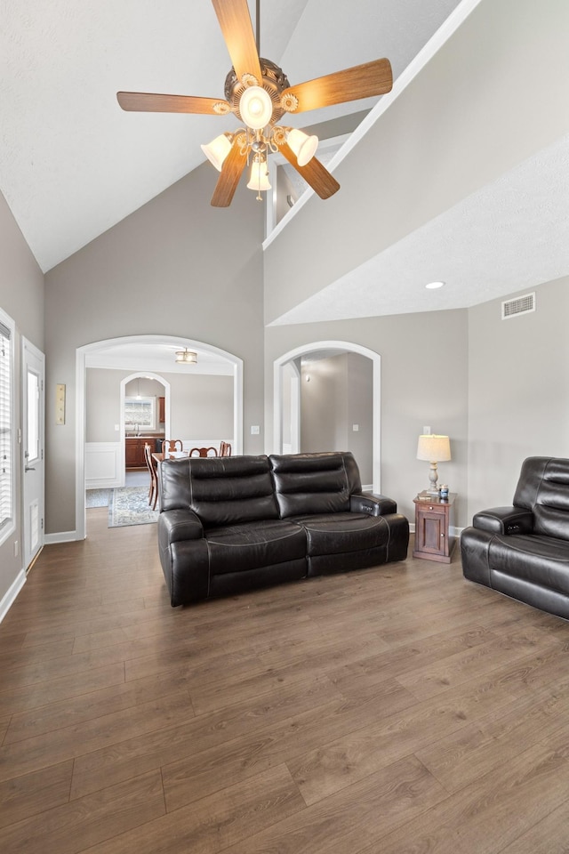 living room with high vaulted ceiling, a ceiling fan, visible vents, arched walkways, and wood finished floors