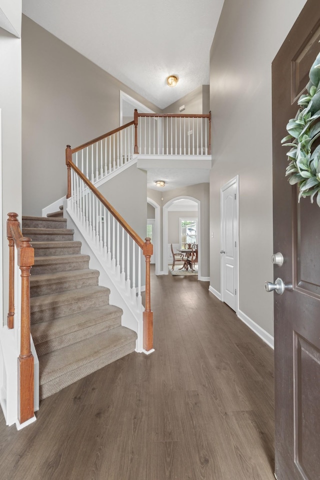 entrance foyer featuring baseboards, stairway, wood finished floors, and arched walkways