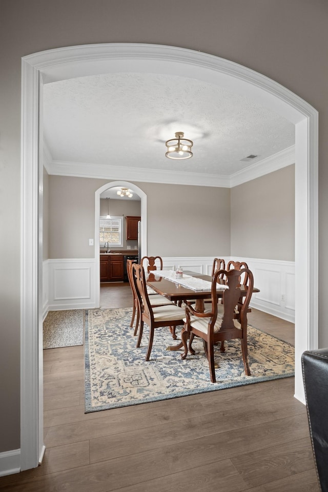 dining space with wainscoting, arched walkways, wood finished floors, and crown molding