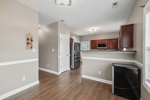 kitchen with dark wood-style flooring, visible vents, a peninsula, baseboards, and appliances with stainless steel finishes
