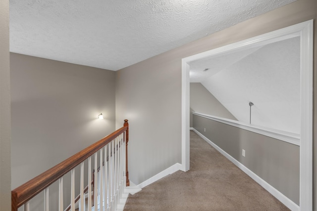 hall with carpet floors, an upstairs landing, baseboards, a textured ceiling, and lofted ceiling