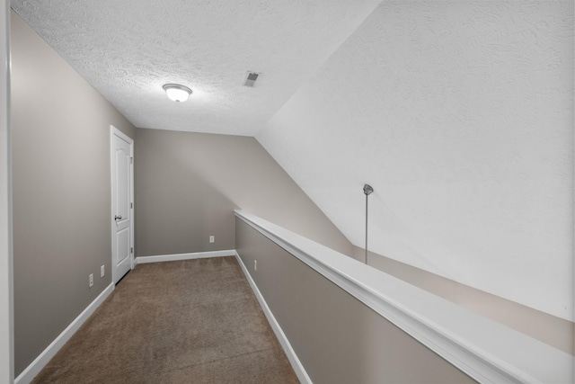hall featuring a textured ceiling, visible vents, baseboards, carpet floors, and vaulted ceiling