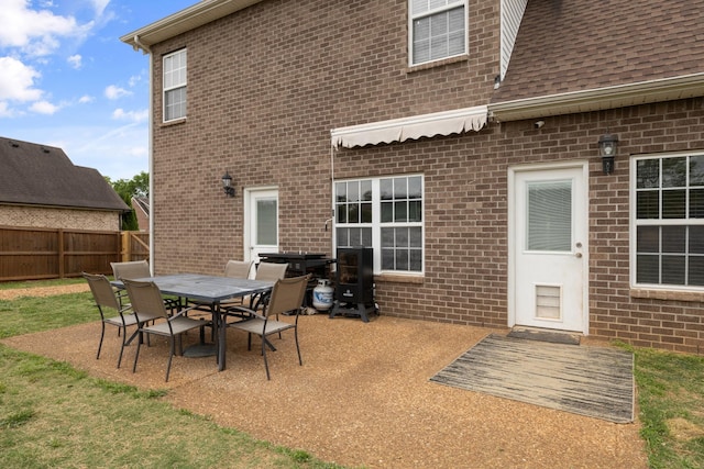 rear view of house featuring a patio, outdoor dining area, roof with shingles, fence, and brick siding