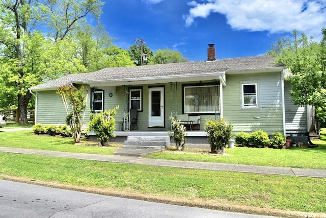 view of front facade with a front yard, covered porch, and a chimney