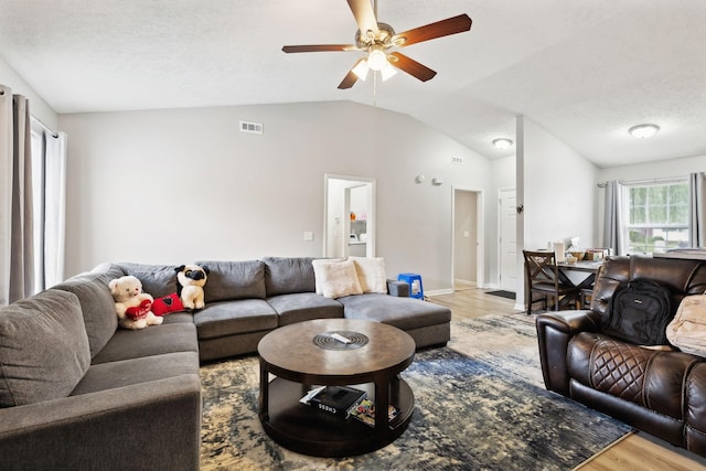 living room with light wood-type flooring, vaulted ceiling, ceiling fan, a textured ceiling, and baseboards